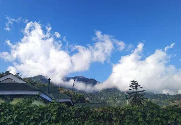 Clouds over forested Aradurah Hill in Kohima, with a green-roofed building in the foreground.